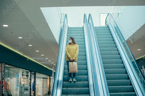 lone woman in a protective mask standing on the escalator steps