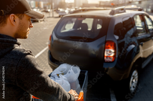 buying food in a supermarket. Shopping A young man buys food for a week in a large shopping center in the countryside. Folds bags of vegetables, fruits, meat and dairy products in a car park © Vlad