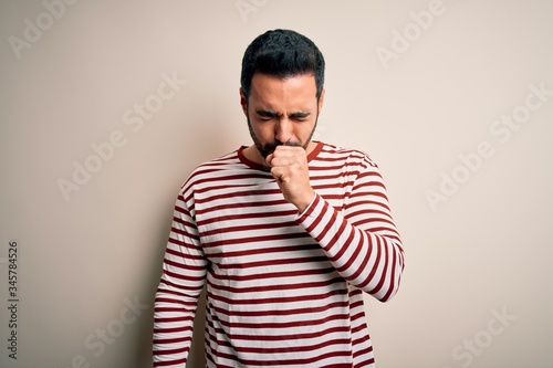 Young handsome man with beard wearing casual striped t-shirt standing over white background feeling unwell and coughing as symptom for cold or bronchitis. Health care concept.