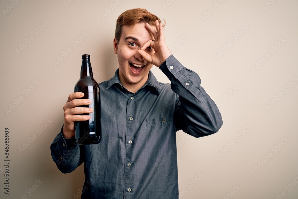 Young handsome redhead man drinking bottle of beer over isolated white background smiling happy doing ok sign with hand on eye looking through fingers Young handsome redhead man drinking bottle of beer over isolated white background smiling happy doing ok sign with hand on eye looking through fingers