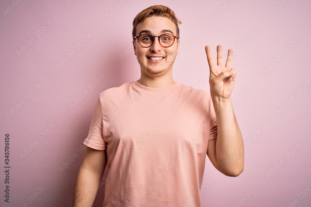 Young handsome redhead man wearing casual t-shirt standing over isolated pink background showing and pointing up with fingers number three while smiling confident and happy. Young handsome redhead man wearing casual t-shirt standing over isolated pink background showing and pointing up with fingers number three while smiling confident and happy.