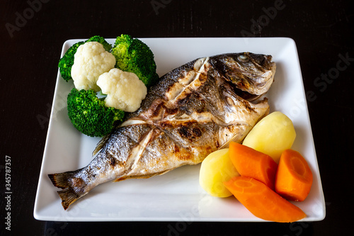 Mediterranean sea dish, Sparus aurata of baked fish vegetables and boiled potatoes on a black background. Healthy food. photo