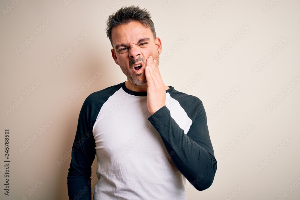 Young handsome man wearing casual t-shirt standing over isolated white background touching mouth with hand with painful expression because of toothache or dental illness on teeth. Dentist Young handsome man wearing casual t-shirt standing over isolated white background touching mouth with hand with painful expression because of toothache or dental illness on teeth. Dentist