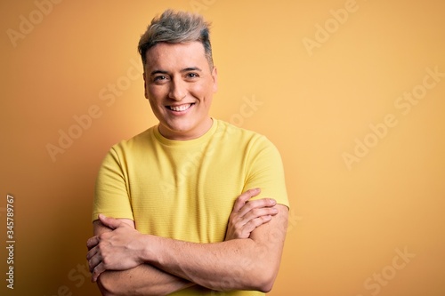 Young handsome modern man wearing yellow shirt over yellow isolated background happy face smiling with crossed arms looking at the camera. Positive person.