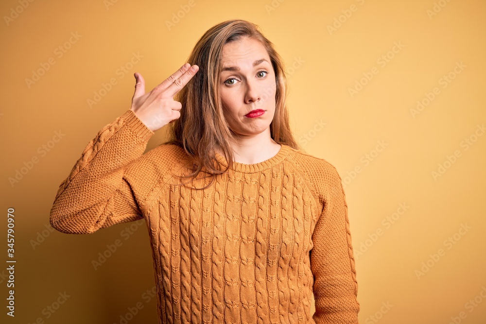 Young beautiful blonde woman wearing casual sweater standing over yellow background Shooting and killing oneself pointing hand and fingers to head like gun, suicide gesture. Young beautiful blonde woman wearing casual sweater standing over yellow background Shooting and killing oneself pointing hand and fingers to head like gun, suicide gesture.