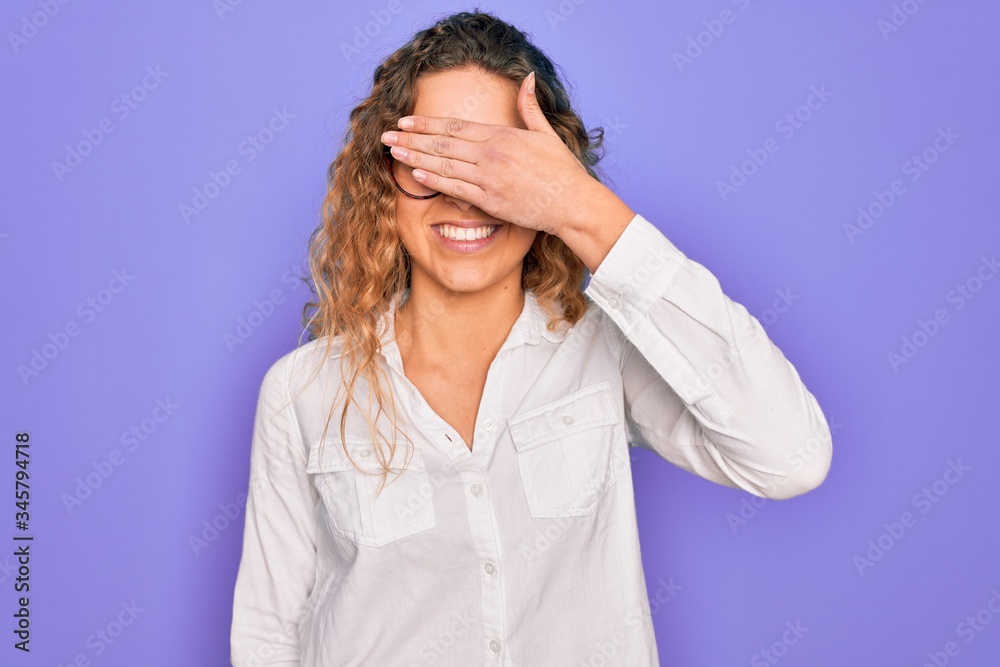 Young beautiful woman with blue eyes wearing casual shirt and glasses over purple background smiling and laughing with hand on face covering eyes for surprise. Blind concept. Young beautiful woman with blue eyes wearing casual shirt and glasses over purple background smiling and laughing with hand on face covering eyes for surprise. Blind concept.