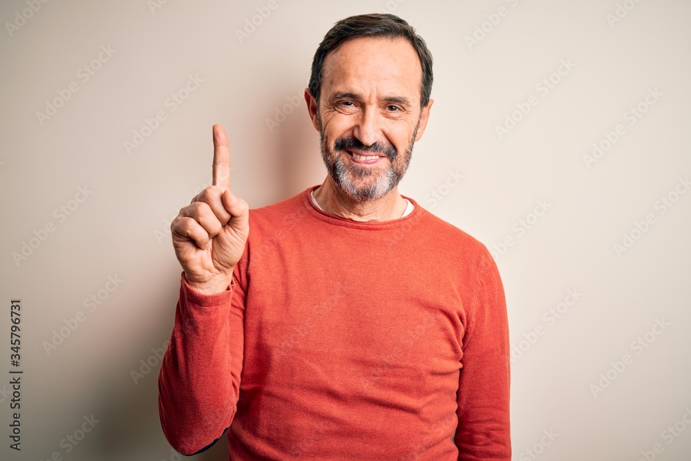 Middle age hoary man wearing casual orange sweater standing over isolated white background showing and pointing up with finger number one while smiling confident and happy.