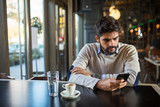 Handsome young bearded man in cafe use phone while waiting someone