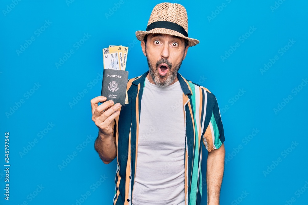 Middle age tourist man on vacation holding united states passport with boarding pass scared and amazed with open mouth for surprise, disbelief face Middle age tourist man on vacation holding united states passport with boarding pass scared and amazed with open mouth for surprise, disbelief face