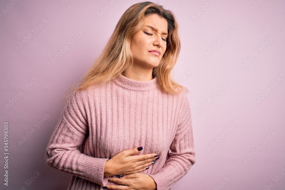 Naklejka premium Young beautiful blonde woman wearing casual pink sweater over isolated background with hand on stomach because indigestion, painful illness feeling unwell. Ache concept.