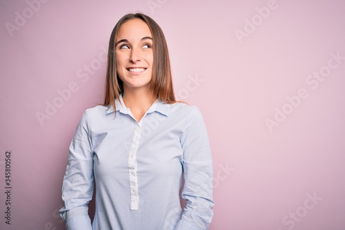 Young beautiful businesswoman wearing elegant shirt standing over isolated pink background looking away to side with smile on face, natural expression. Laughing confident.