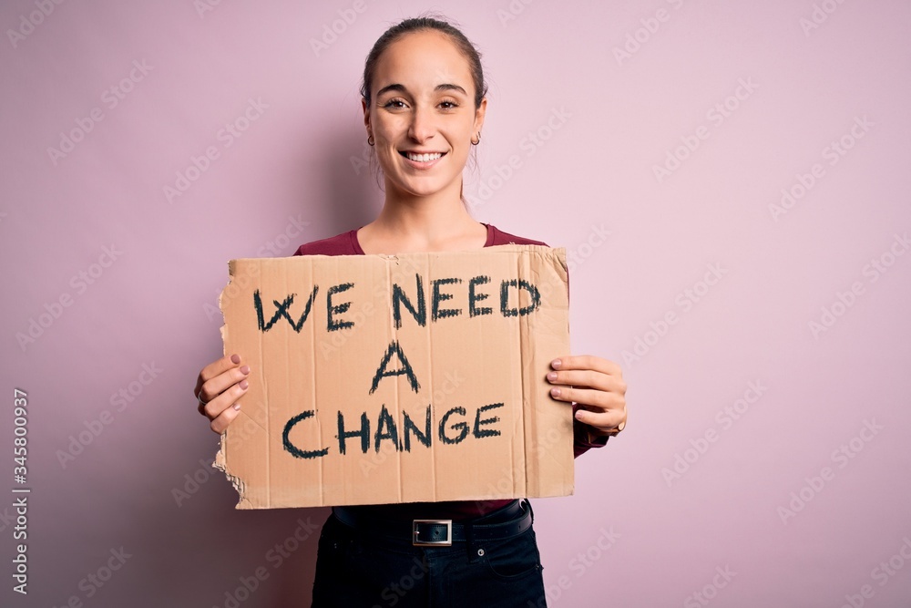 Young beautiful activist woman asking for change protesting holding banner with message with a happy face standing and smiling with a confident smile showing teeth