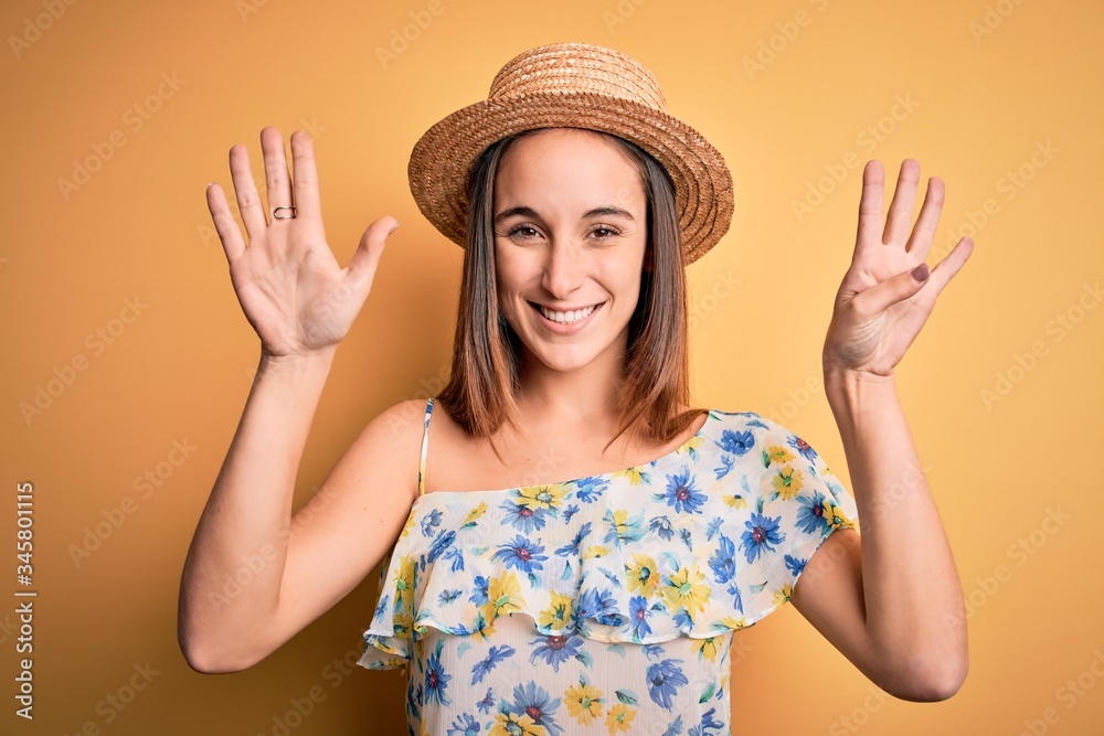 Young beautiful woman wearing casual t-shirt and summer hat over isolated yellow background showing and pointing up with fingers number nine while smiling confident and happy.