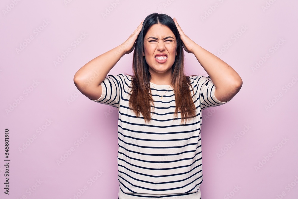 Young beautiful brunette woman wearing casual striped t-shirt over isolated pink background with hand on head, headache because stress. Suffering migraine. Young beautiful brunette woman wearing casual striped t-shirt over isolated pink background with hand on head, headache because stress. Suffering migraine.
