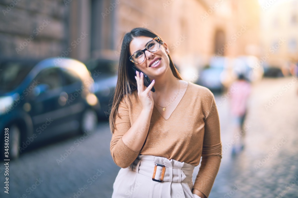 Fototapeta premium Young beautiful woman smiling happy and confident. Standing with smile on face talking by the smartphone at the city