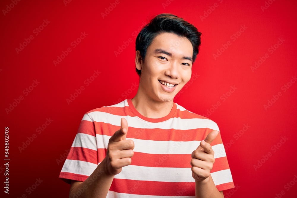 Young handsome chinese man wearing casual striped t-shirt standing over red background pointing fingers to camera with happy and funny face. Good energy and vibes. Young handsome chinese man wearing casual striped t-shirt standing over red background pointing fingers to camera with happy and funny face. Good energy and vibes.