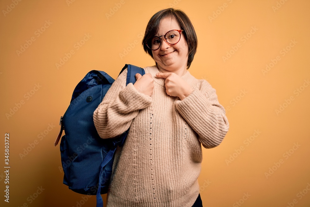 Obraz premium Young down syndrome student woman wearing school bag over yellow background very happy pointing with hand and finger