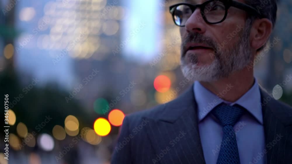 Mature businessman in elegant suit walking at urban setting in metropolitan city using modern cellular gadget for checking online news about corporate project happy with approved result
