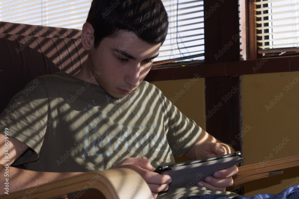 Caucasian boy sitting in an armchair checks his social networks on the tablet