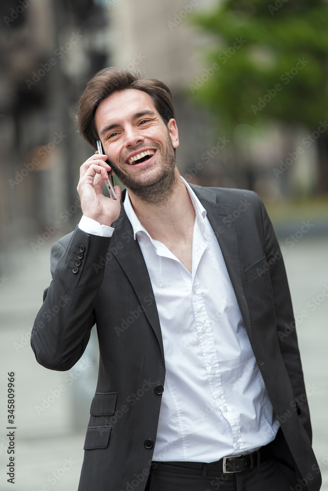 Attractive young businessman having a pleasant phone talk while walking in the urban part of the city Attractive young businessman having a pleasant phone talk while walking in the urban part of the city
