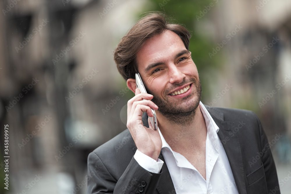 Attractive young businessman having a pleasant phone talk while walking in the urban part of the city Attractive young businessman having a pleasant phone talk while walking in the urban part of the city