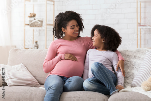 Young black pregnant woman bonding with her little daughter at home