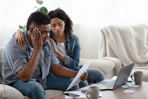 Financial Crisis. Depressed black couple sitting with huge bills in living room © Prostock-studio