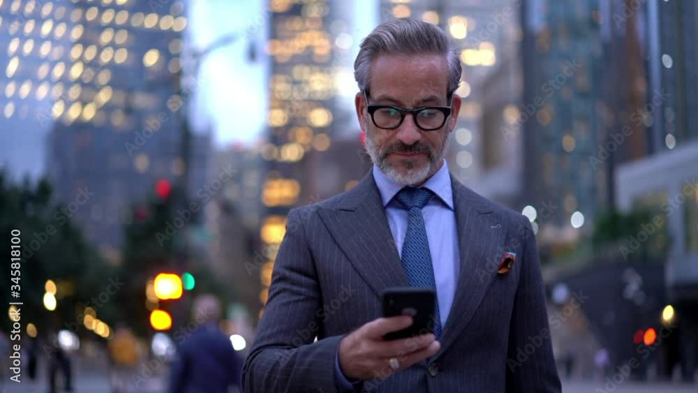 Mature male employer formally dressed typing text message for send via smartphone device, slow motion effect of middle aged businessman in eyeglasses using mobile device for phoning outdoors
