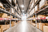 Blurred view of the interior of a warehouse; boxes stacked up high on both sides of an aisle
