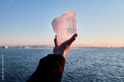 Man holdning a block of Greenlandic inland ice in the sunset photo