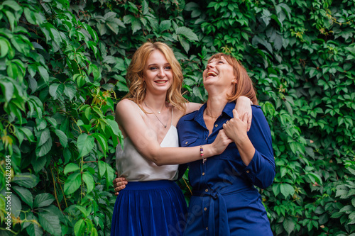 Beautiful mother and her grown up daughter hugging each other and laughing on a summer day outside