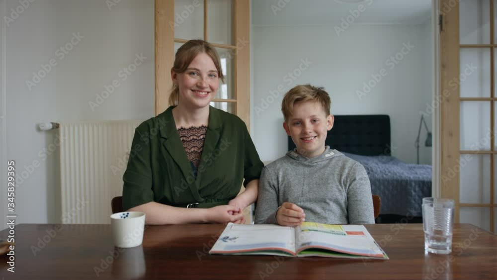 Lille brother and big sister doing home work together looks into the camera and smiles with wide dolly track in. They are in the living room with a book on the table. Lille brother and big sister doing home work together looks into the camera and smiles with wide dolly track in. They are in the living room with a book on the table.
