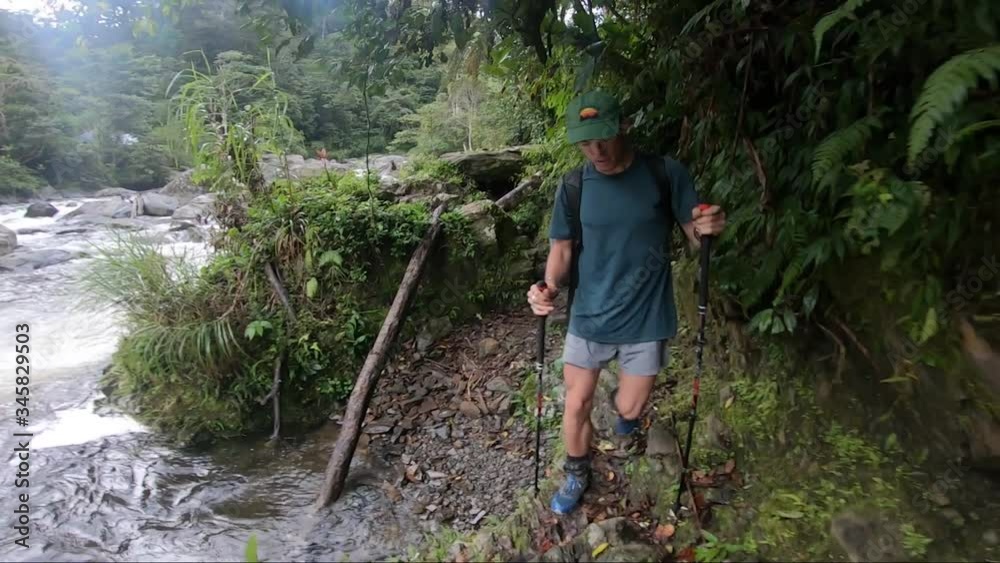 A young man is hiking up a small trail next to a big river running down with power in the tropical jungle of Papa New Guinea. A young man is hiking up a small trail next to a big river running down with power in the tropical jungle of Papa New Guinea.