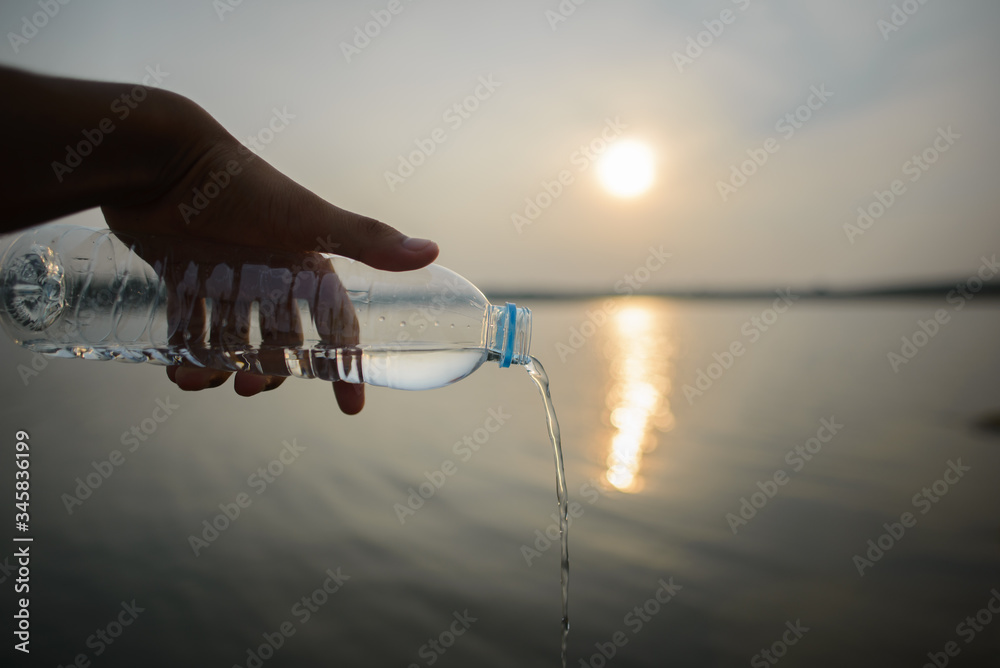 A man holds a glass of water bottle that can be reused without writing on plastic on the beach with the ocean behind.