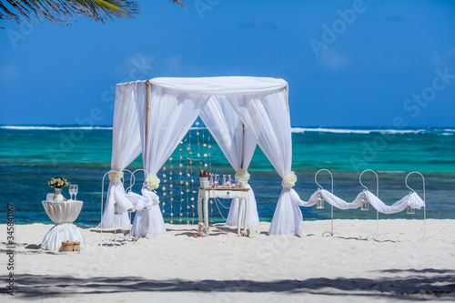 Fototapeta Naklejka Na Ścianę i Meble -  Colorful wedding arch gazebo pavilion made of bamboo and textile with fresh flowers decoration at sandy beach on sunny day for destination wedding ceremony in Dominican republic  