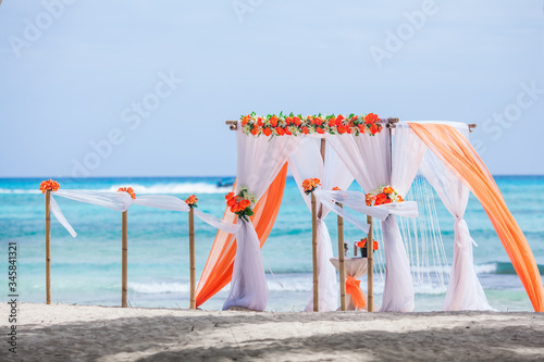 Colorful wedding arch gazebo pavilion made of bamboo and textile with fresh flowers decoration at sandy beach on sunny day for destination wedding ceremony in Dominican republic 