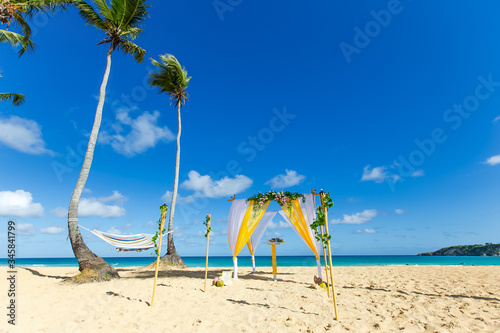 Colorful wedding arch gazebo pavilion made of bamboo and textile with fresh flowers decoration at sandy beach on sunny day for destination wedding ceremony in Dominican republic 