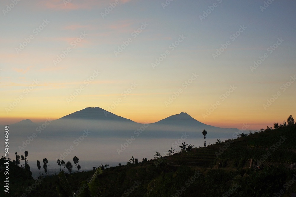 view of Mount Sindoro at sunrise with the background of Mount Merapi Merbabu covered in white clouds. Photo taken in July 2019