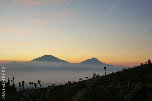 view of Mount Sindoro at sunrise with the background of Mount Merapi Merbabu covered in white clouds. Photo taken in July 2019