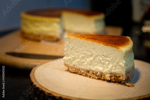 New York cheesecake slice on wooden plate on black counter in kitchen room. Concept for homemade bakery