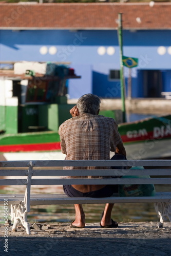 Elderly man sitting on park bench watched boats on a river