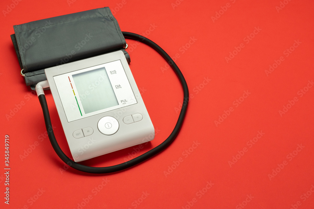 Blood pressure check. Health monitor for check doctor blood pressure isolated on red background. Patient test hypertension from medical sphygmomanometer. Hospital diagnostic technology. Blood pressure check. Health monitor for check doctor blood pressure isolated on red background. Patient test hypertension from medical sphygmomanometer. Hospital diagnostic technology.