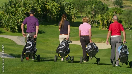 WS Four golfers with golf bags walking down hill on golf course