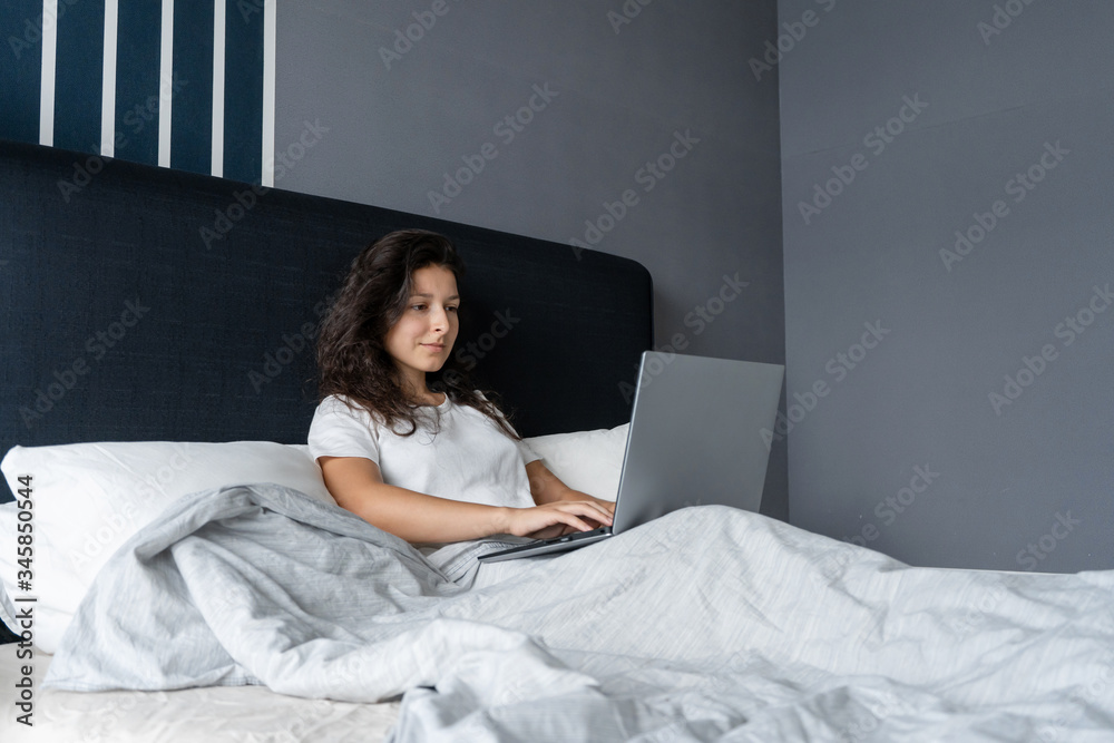 Beautiful brunette girl in bed with a laptop. Work from morning to late night. Electronic gadgets before bedtime or in the morning. Beautiful brunette girl in bed with a laptop. Work from morning to late night. Electronic gadgets before bedtime or in the morning.