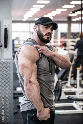 strong young bearded man showing big triceps muscle during posing in sport gym after hard workout
