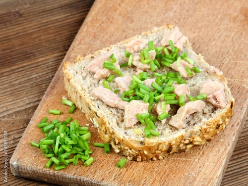 Cod liver over brown bread with spring  green onion. Healthy cod liver on whole grain bread,  wooden cutting board.