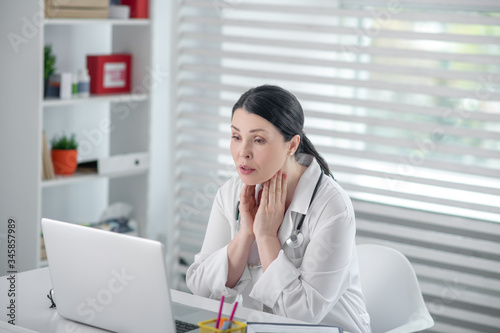 Successful woman in white coat in front of laptop.