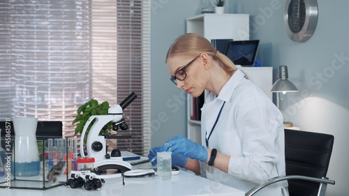 Chemistry scientist examining substance under magnifying glass after taking it from slider with pipette