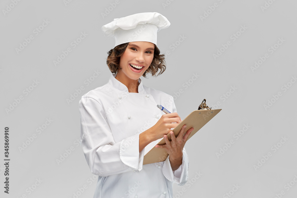 cooking, culinary and people concept - happy smiling female chef in toque with clipboard and pen over grey background cooking, culinary and people concept - happy smiling female chef in toque with clipboard and pen over grey background