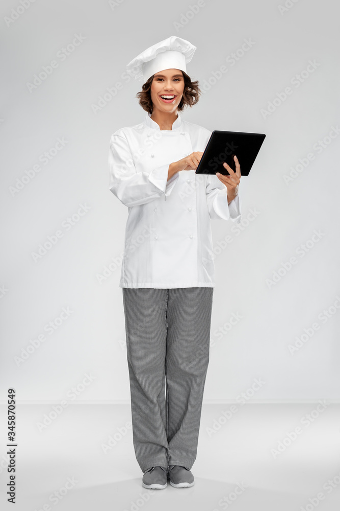 cooking, culinary and people concept - happy smiling female chef in toque with tablet pc computer over grey background